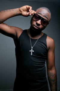 A young Davido wearing a black tank top, sunglasses, and a large silver cross pendant necklace during his early music career breakout in Nigeria.